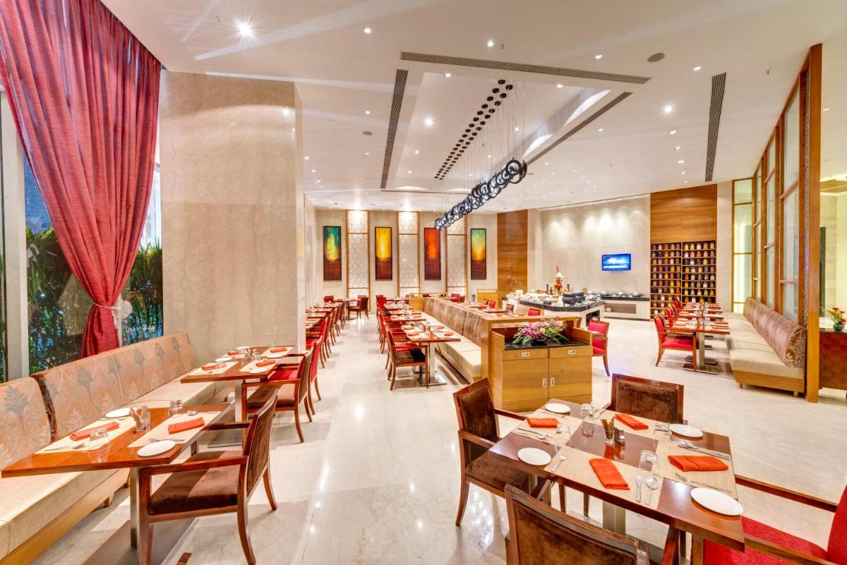 a restaurant with wooden tables and chairs and a large window at Pride Plaza Hotel, Kolkata in Kolkata