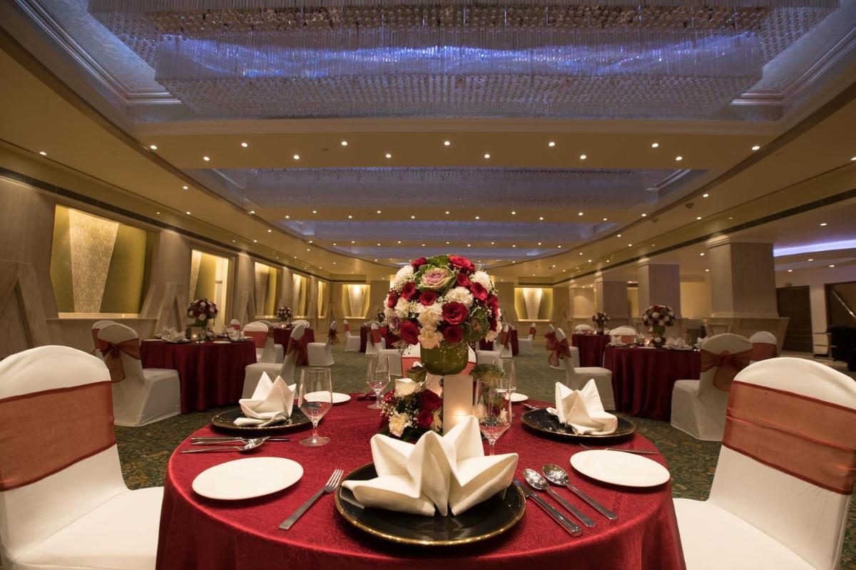 a banquet hall with a table with red table cloth and flowers at The Suryaa New Delhi in New Delhi a banquet hall with a table with red table cloth and flowers at The Suryaa New Delhi in New Delhi