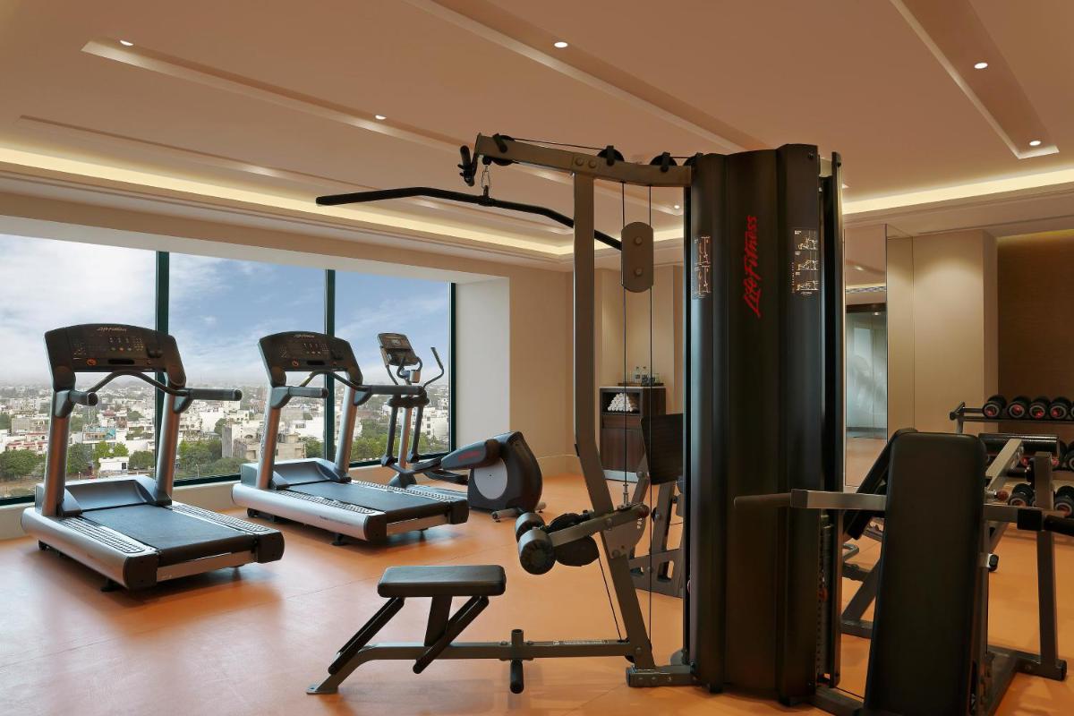 a gym with several exercise equipment in a room with windows at Novotel Lucknow Gomti Nagar in Lucknow