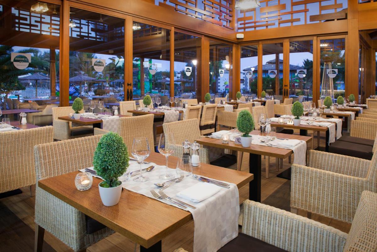 Un restaurante con mesas, sillas y ventanas. en Elba Lanzarote Royal Village Resort, en Playa Blanca