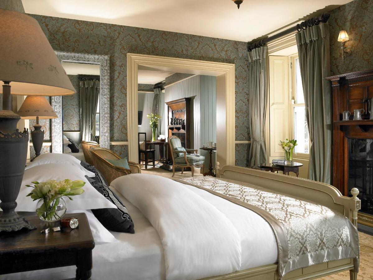 Elegant hotel room with vintage decor, a large bed, seating area, and natural light from tall windows.
