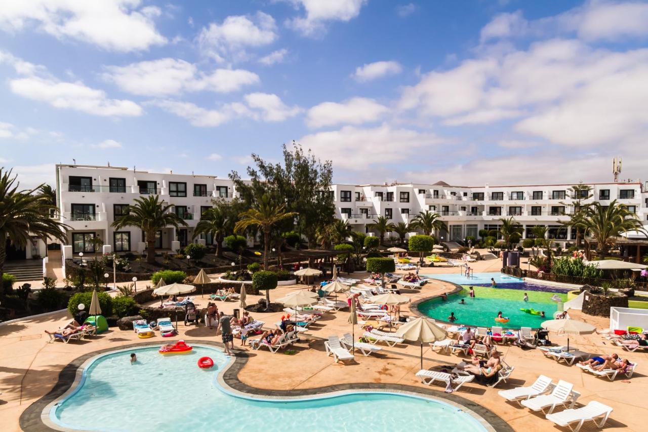 A sunny resort with pools, lounge chairs, and white buildings surrounded by palm trees.
