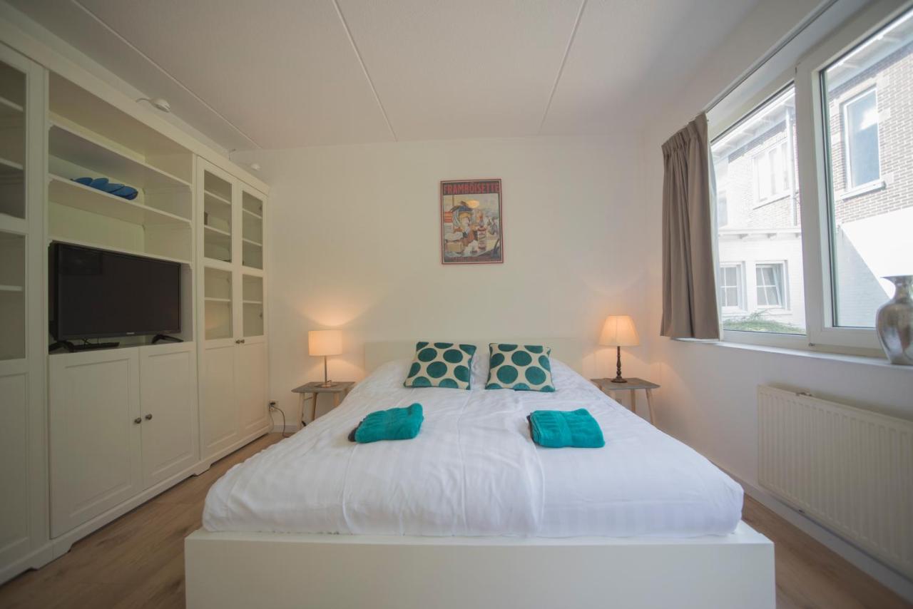 a white bedroom with a large bed with blue pillows at Amsterdam Beach in Zandvoort