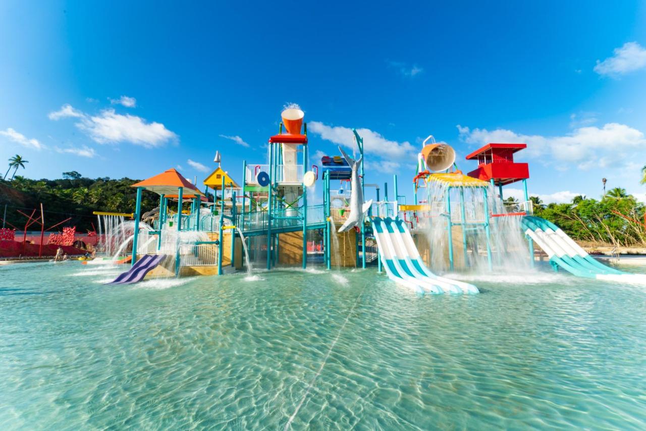 Grande piscina rasa e grande parque aquático infantil com dois baldões e vários escorregadores.