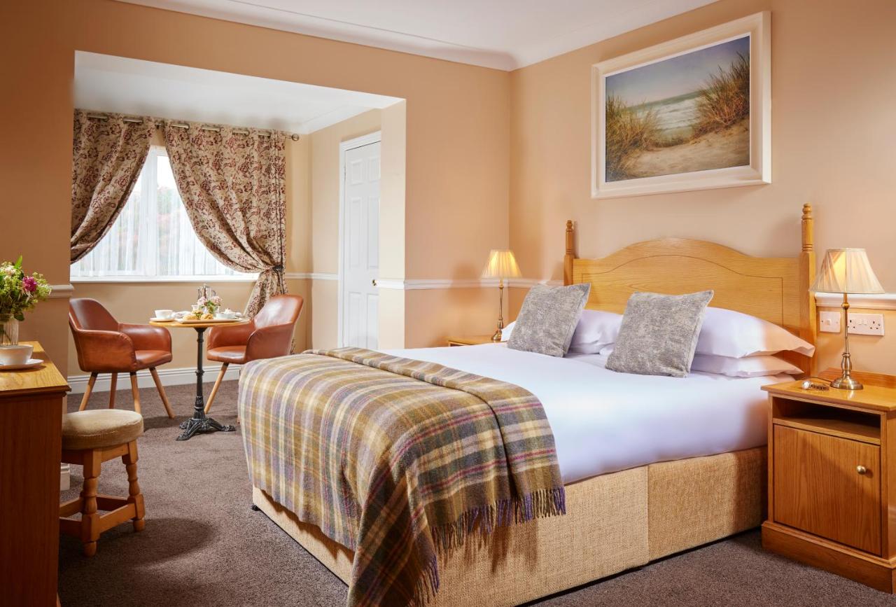 Cozy hotel room with double bed, two chairs, a table by the window, and a nature painting on the wall.