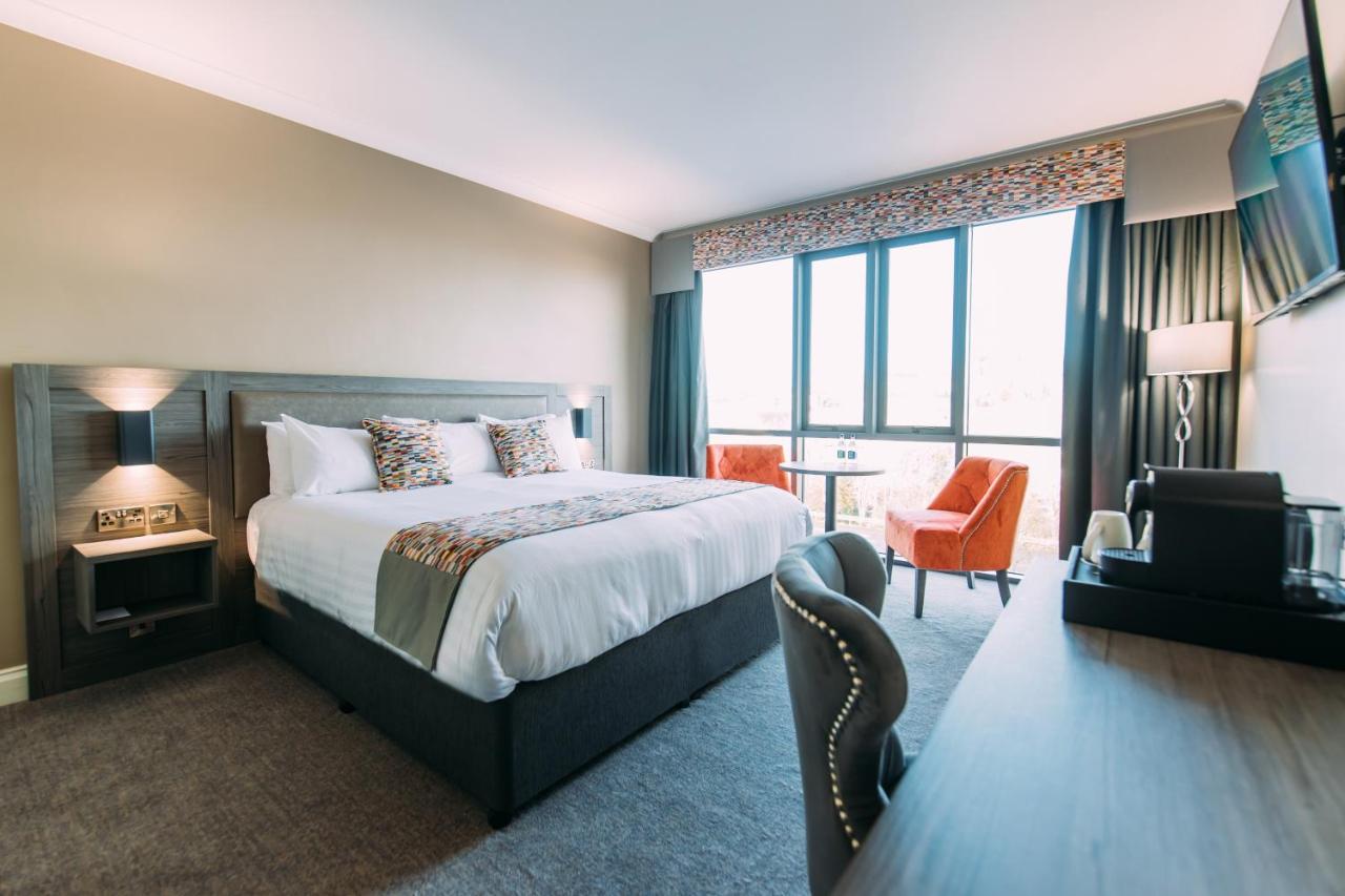 Modern hotel room with a large bed, desk, and small seating area by the window.