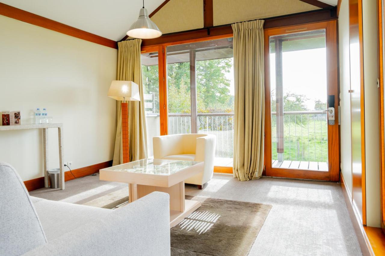 a living room with a table and chairs and windows at Le Manoir du Lys, The Originals Relais in Bagnoles de l'Orne