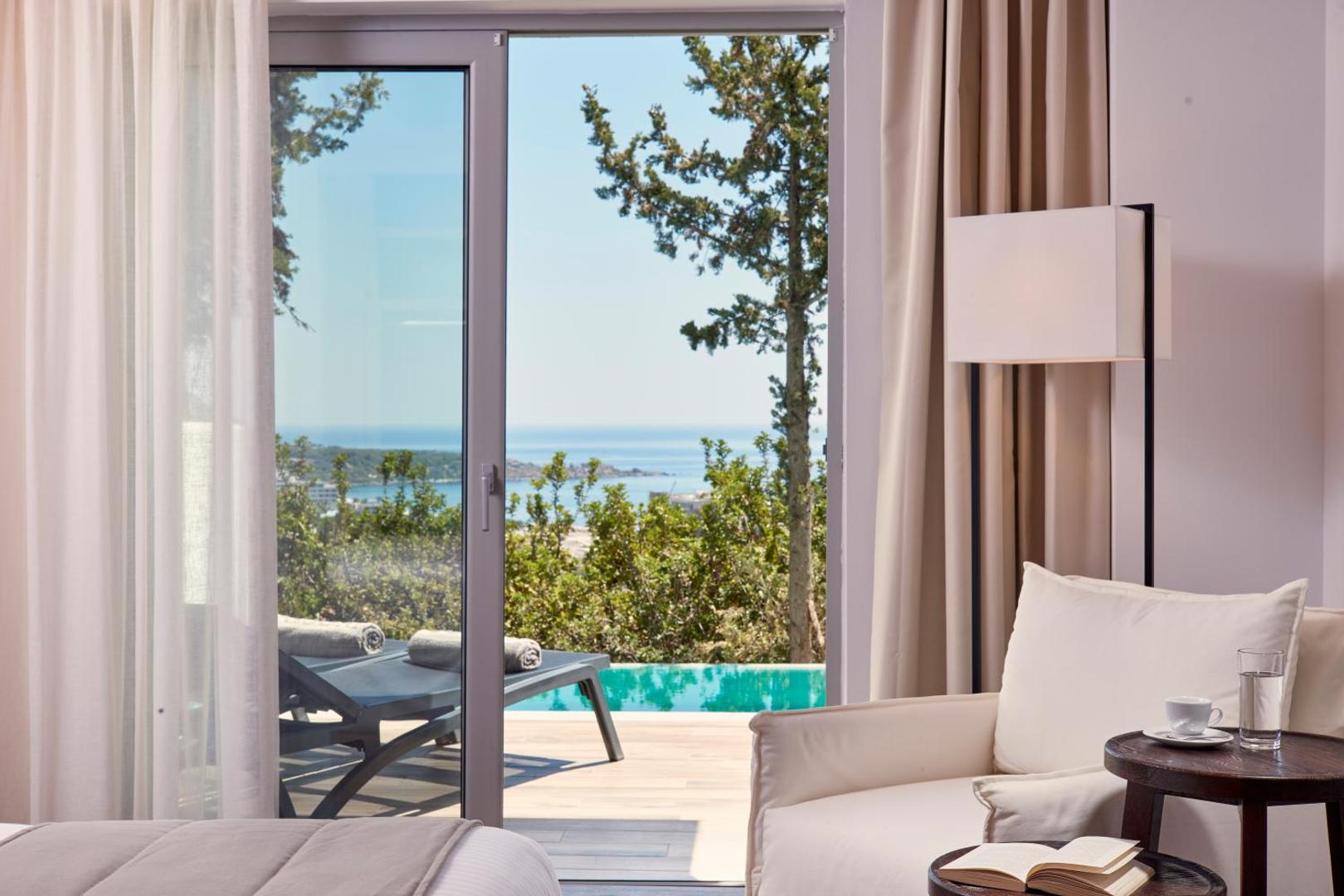 Skats no numura iekšpuses uz terasi ar sauļošanās krēsliem un baseinu.