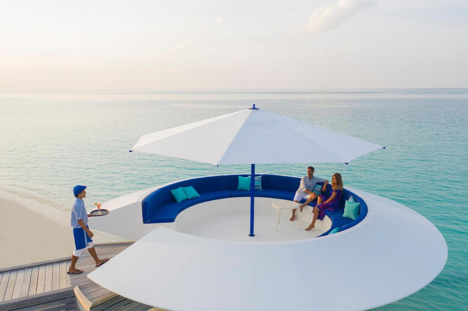 Pāris atpūšas uz unikālas, apaļas platformas ar saulessargu okeāna piekrastē.