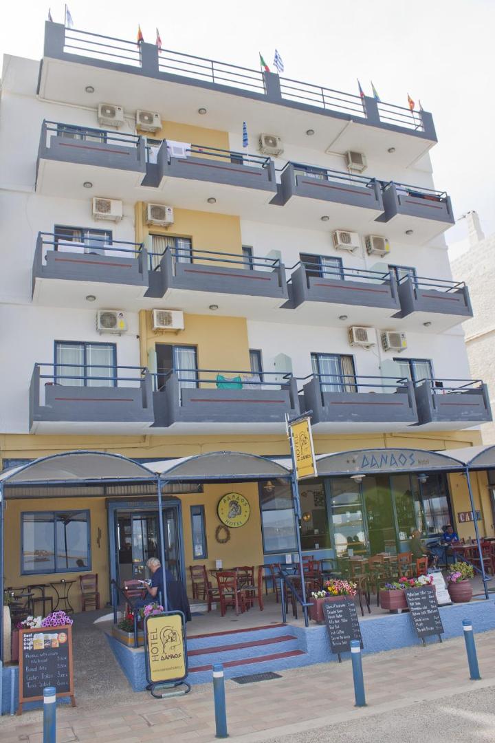Danaos Beach Apartments daudzstāvu ēkas fasāde ar balkoniem un āra kafejnīcu pirmajā stāvā.