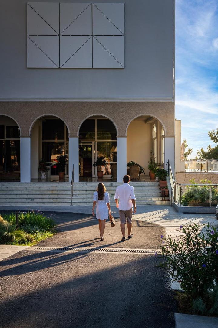 Pāris dodas iekšā viesnīcas galvenajā ieeja ar arkveida logiem saules gaismā.