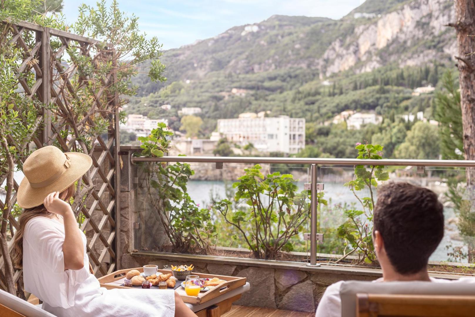 Pāris bauda brokastis uz balkona ar skatu uz ciematu un kalniem.