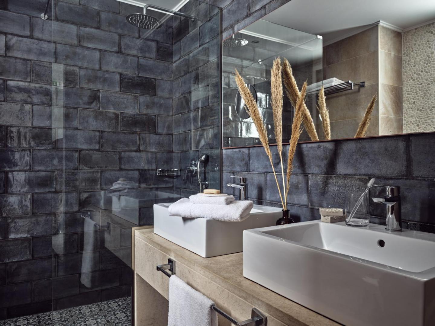 Moderna vannas istaba ar tumšām flīzēm, divām izlietnēm un stikla dušas kabīni.