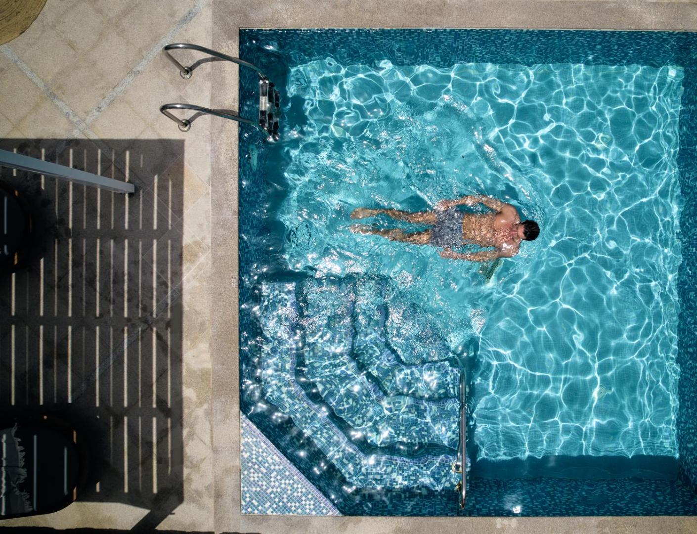 Skats no augšas uz vīrieti, kurš peldas dzidrā, zilā flīžu baseinā.