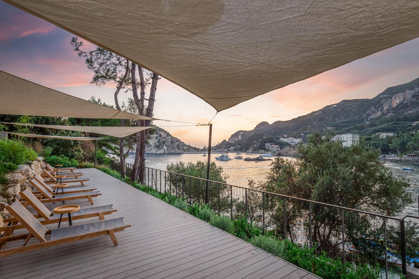 Koka terase ar sauļošanās krēsliem un nojumēm saulrieta gaismā.