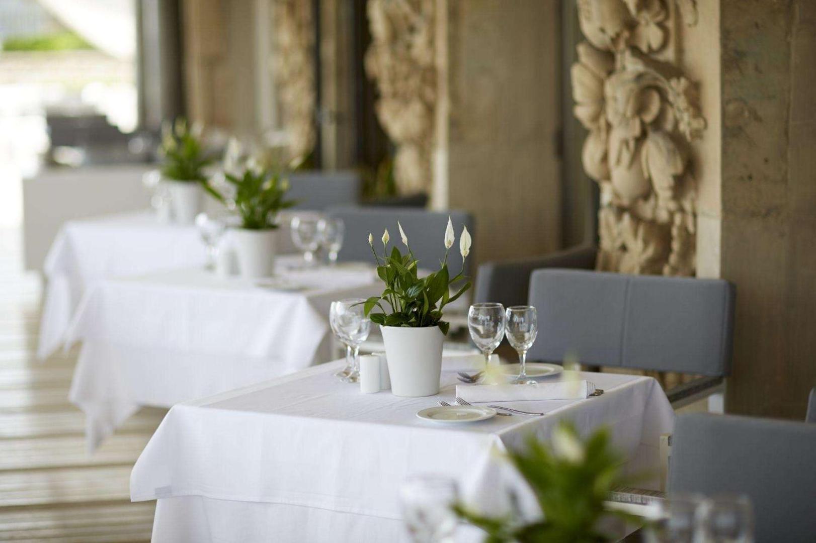 Tuvplāns restorāna galdam ar baltu galdautu, ziedu dekoru un vīna glāzēm.