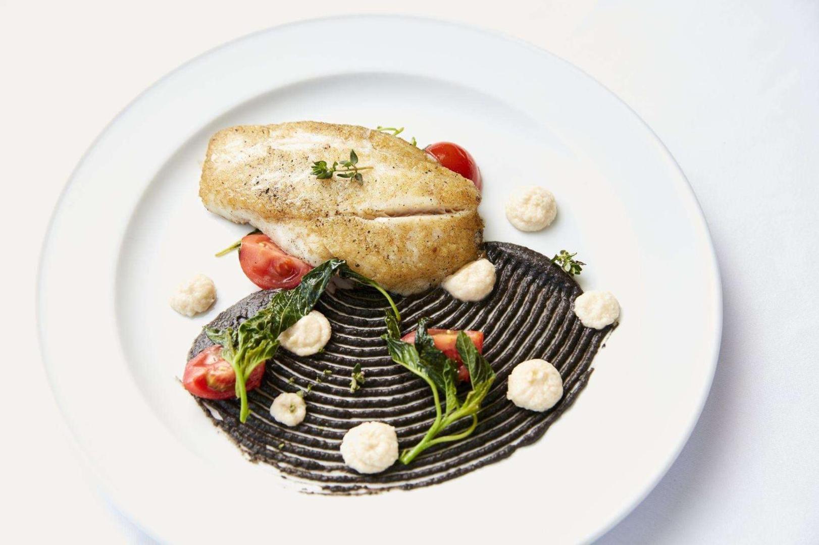 Cepta zivs fileja ar dārzeņiem un dekoratīvu mērci uz apaļa šķīvja.