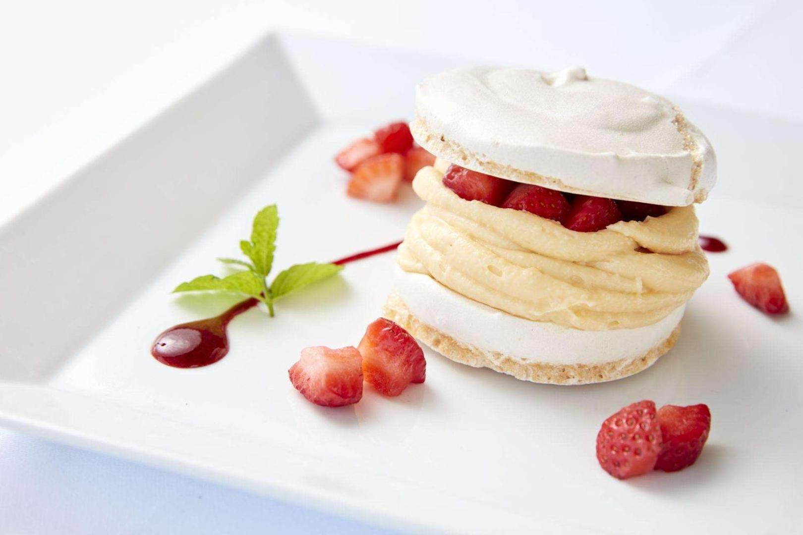 Gaisīgs bezē deserts ar krēmu un svaigām zemenēm uz balta šķīvja.