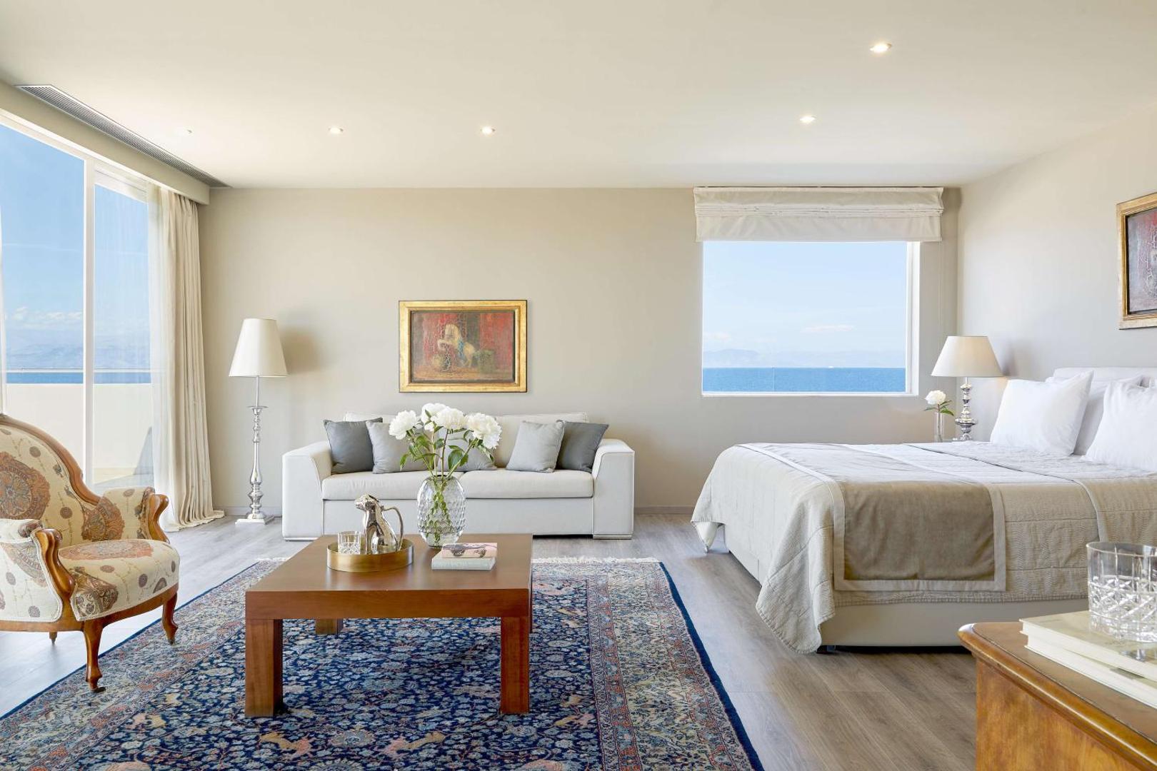 Gaišs un elegants viesnīcas numurs ar lielu gultu, dīvānu un skatu uz jūru.