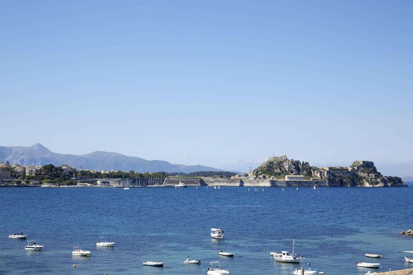 Panorāmas skats uz zilo Jonijas jūru un vēsturisko Korfu vecpilsētas cietoksni tālumā.