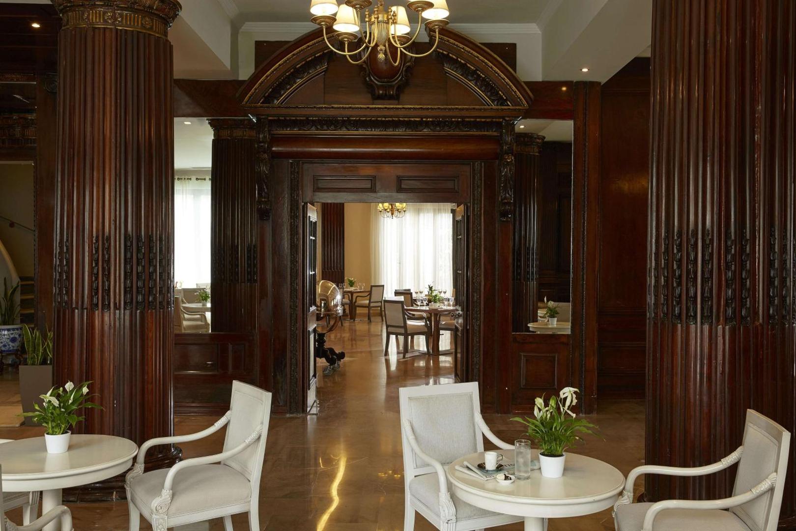 Viesnīcas Mon Repos Palace vestibils ar tumša koka paneļiem, kolonnām un baltiem atpūtas krēsliem.