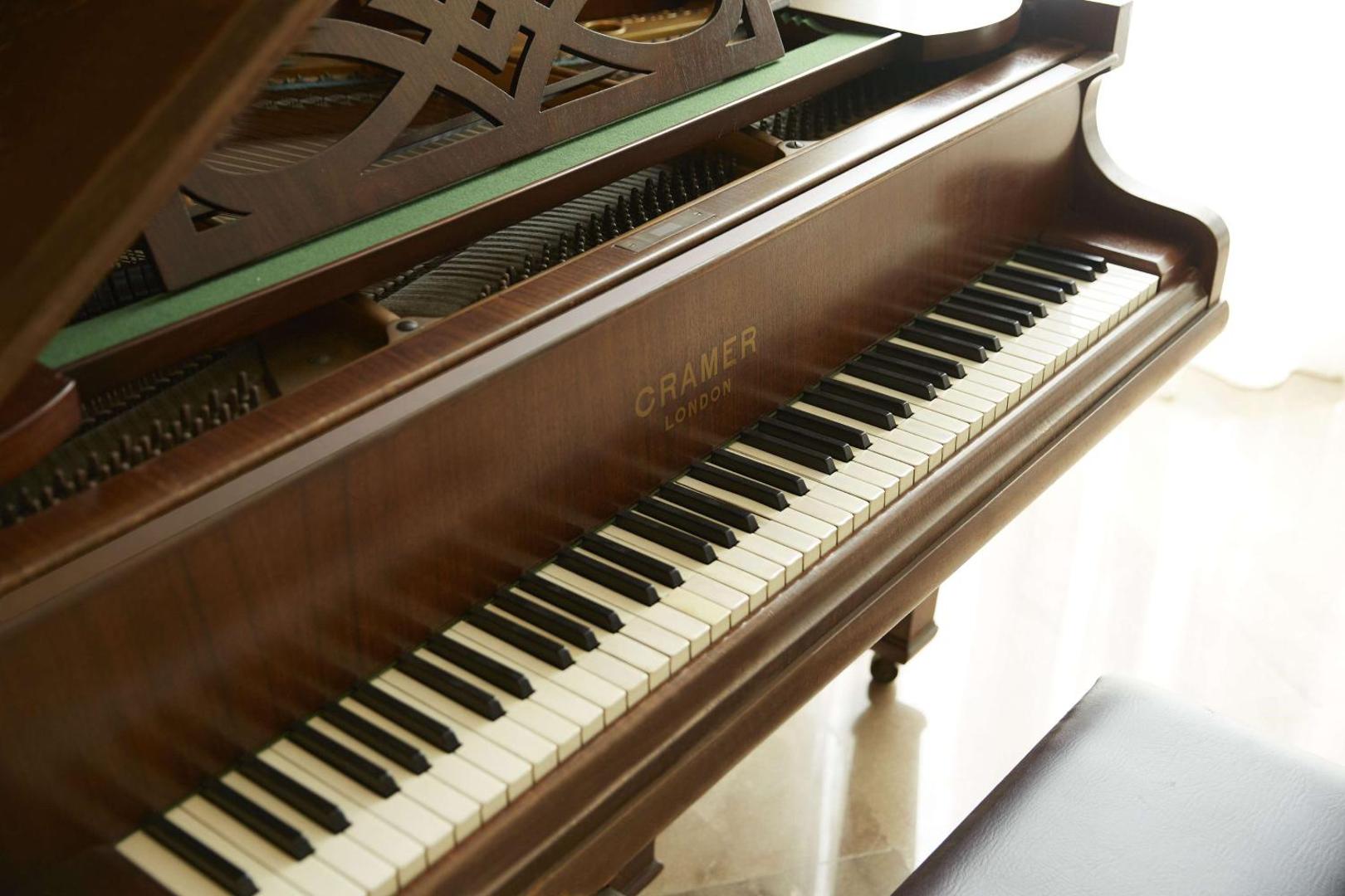 Klasisks koka flīģelis Cramer London gaišā telpā pie loga.