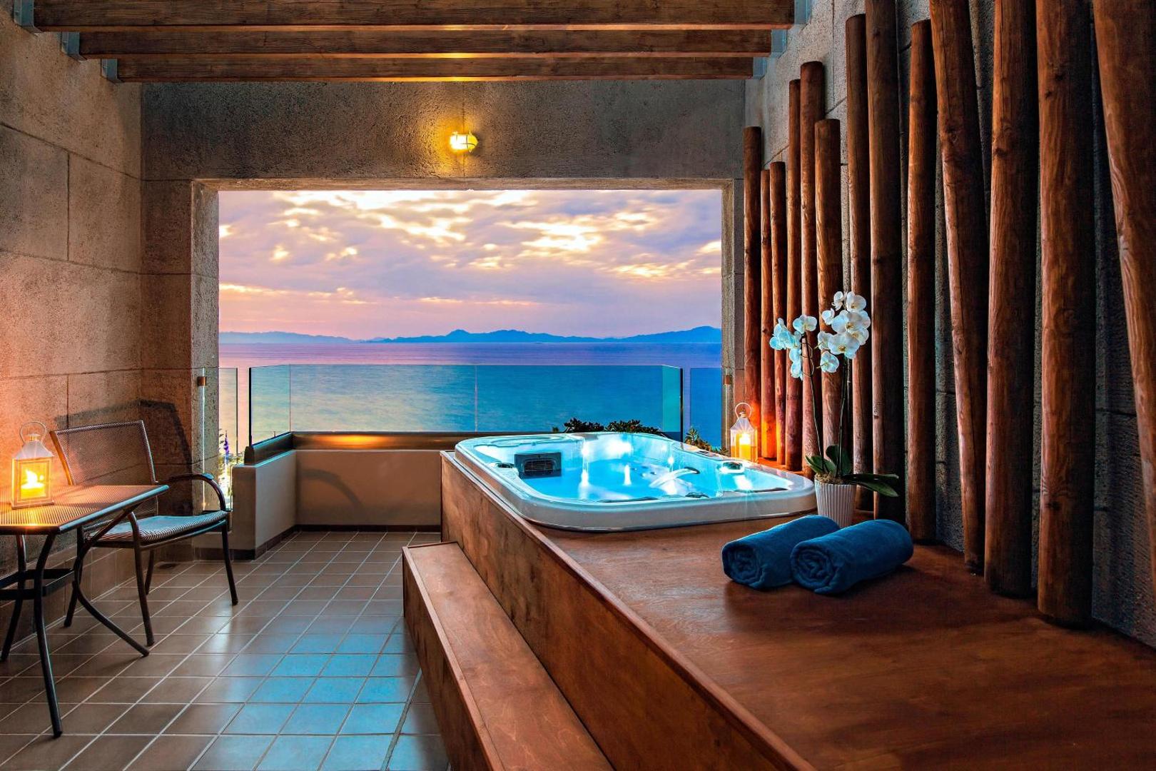 Privāta terase ar džakuzi, no kuras paveras skats uz jūru saulrietā.