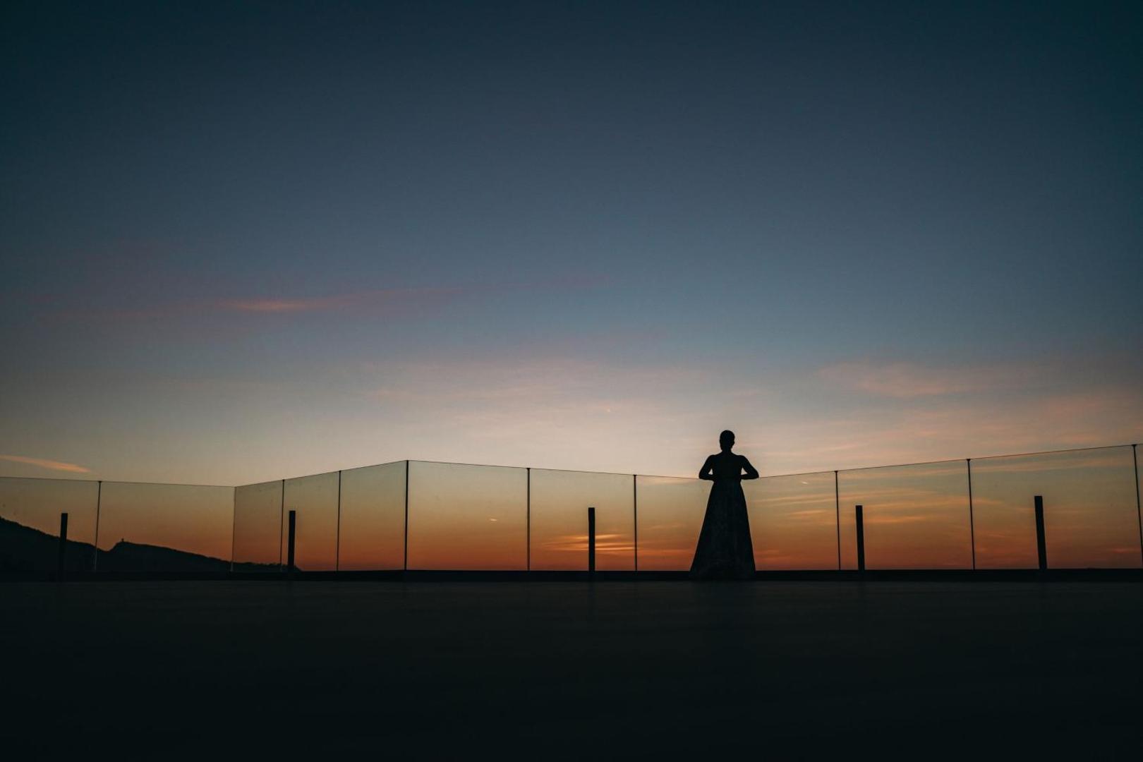 Sievietes siluets uz terases saulrieta laikā ar skatu uz horizontu.