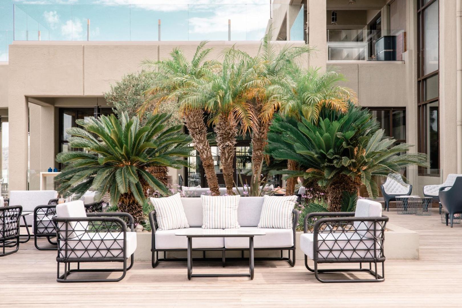Āra atpūtas zona ar modernām mēbelēm, dīvāniem un palmām uz koka terases.