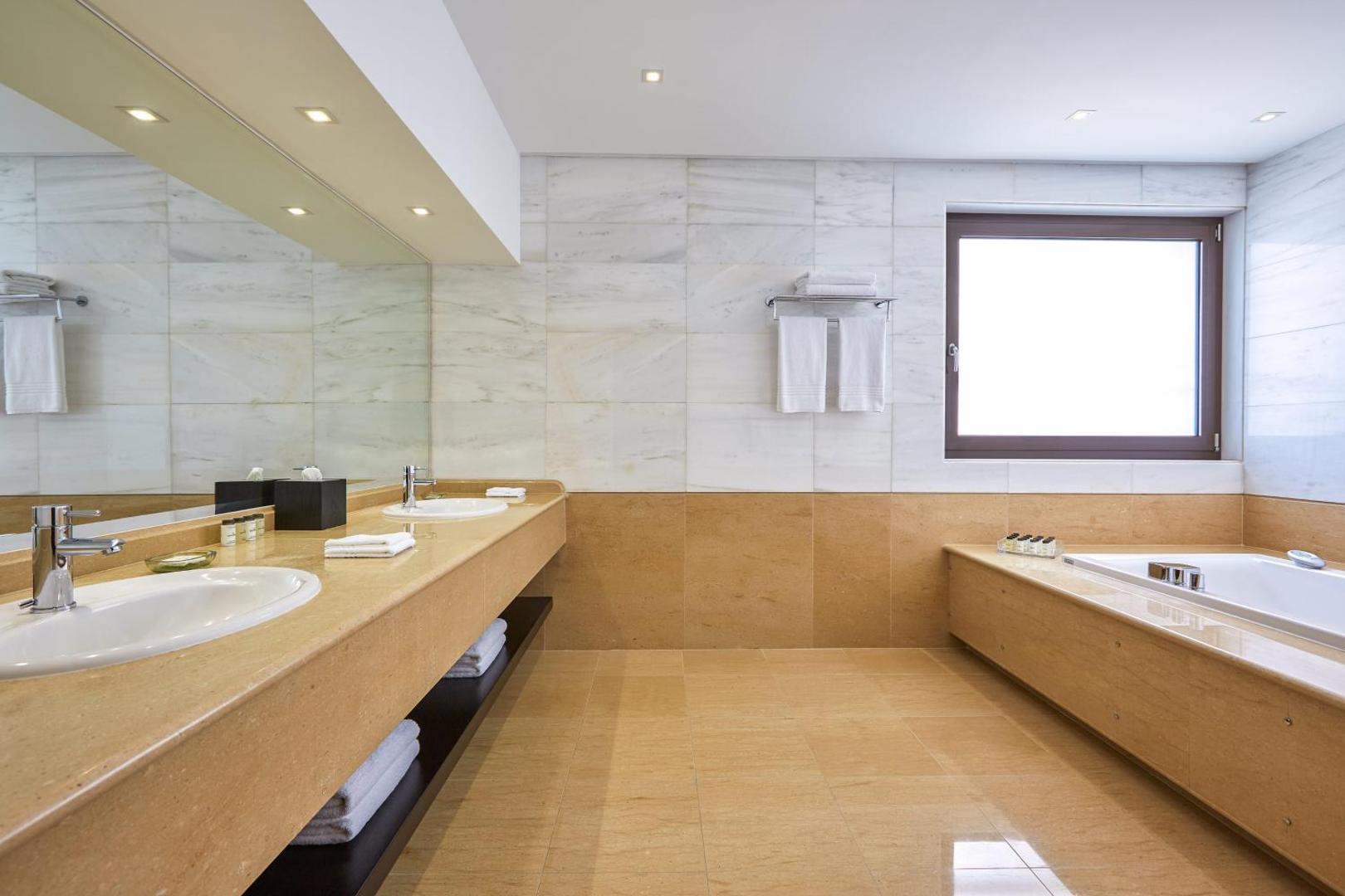 Plaša vannas numura interjers ar divām izlietnēm, lielu spoguli un iebūvētu vannu.