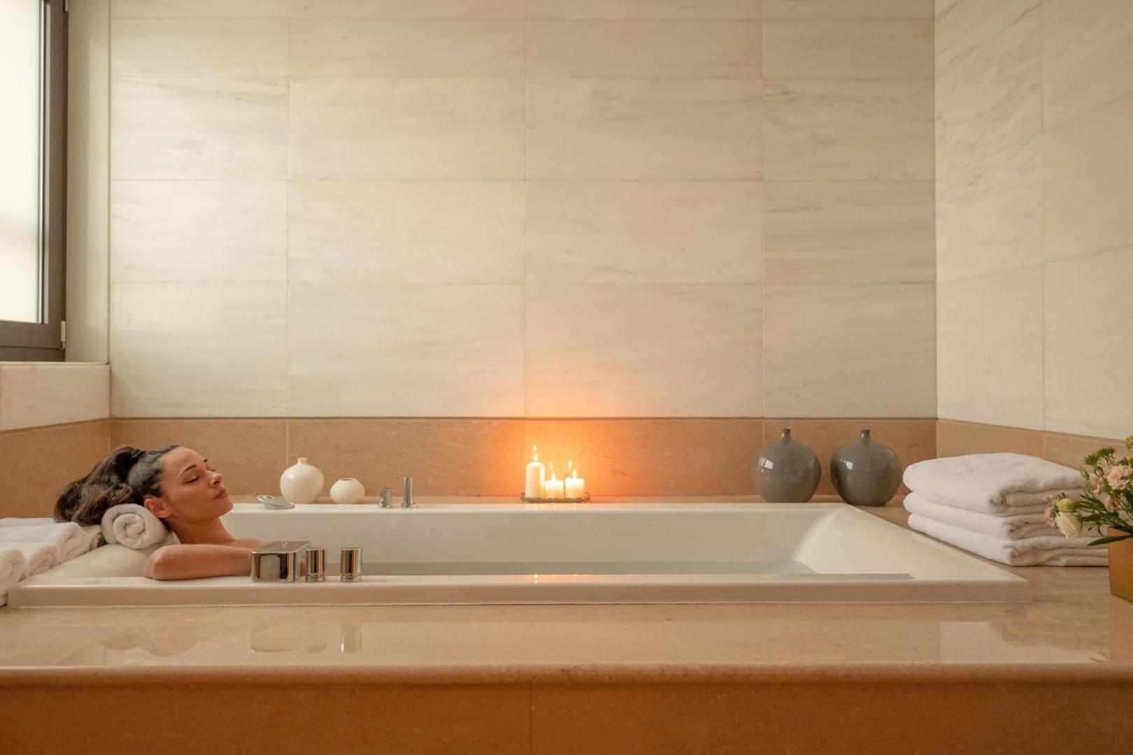Sieviete relaksējas vannā Sheraton Rhodes Resort marmora vannas istabā.