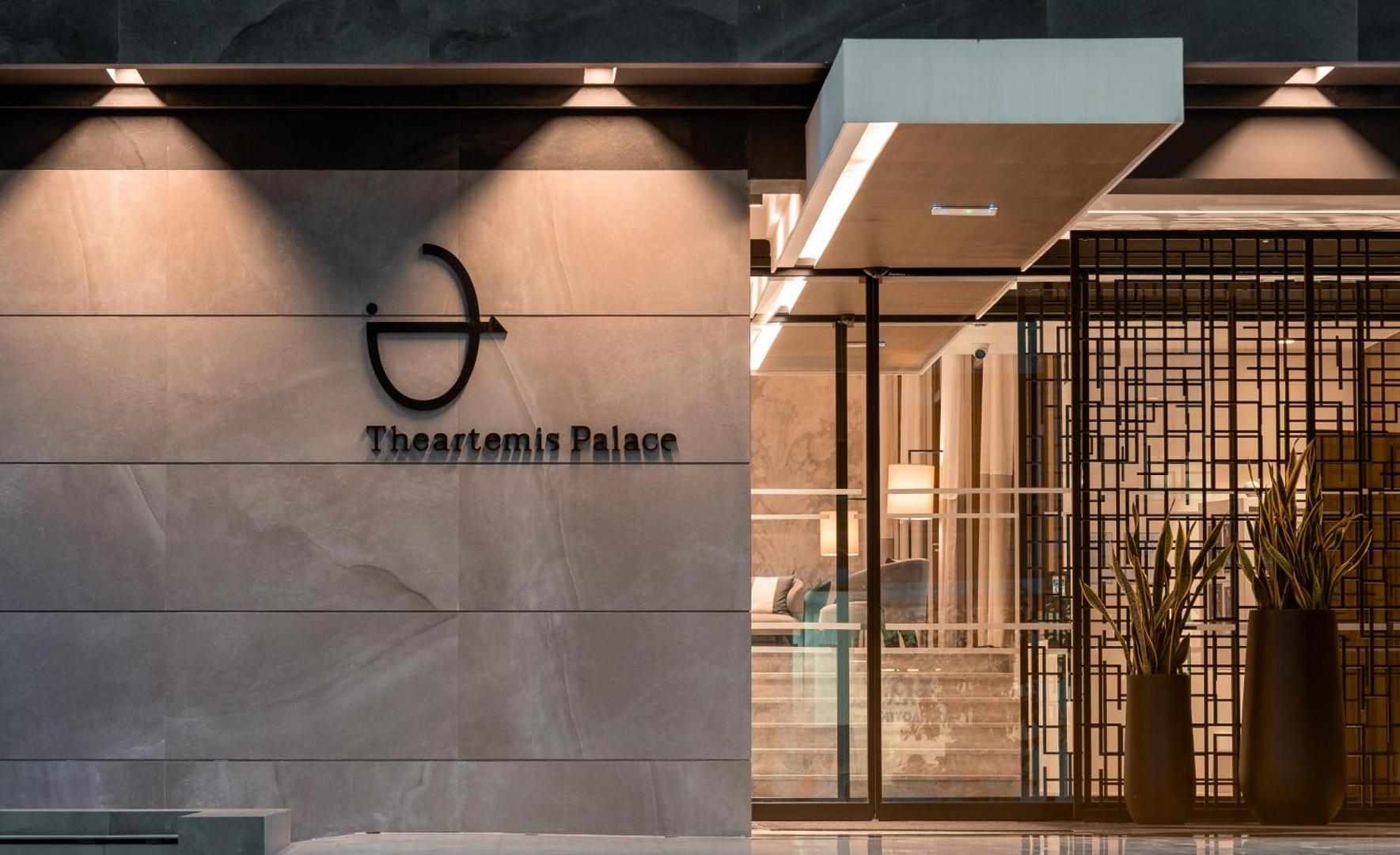 Theartemis Palace viesnīcas ieejas zīme un modernais vestibils vakarā ar siltu apgaismojumu un stikla durvīm