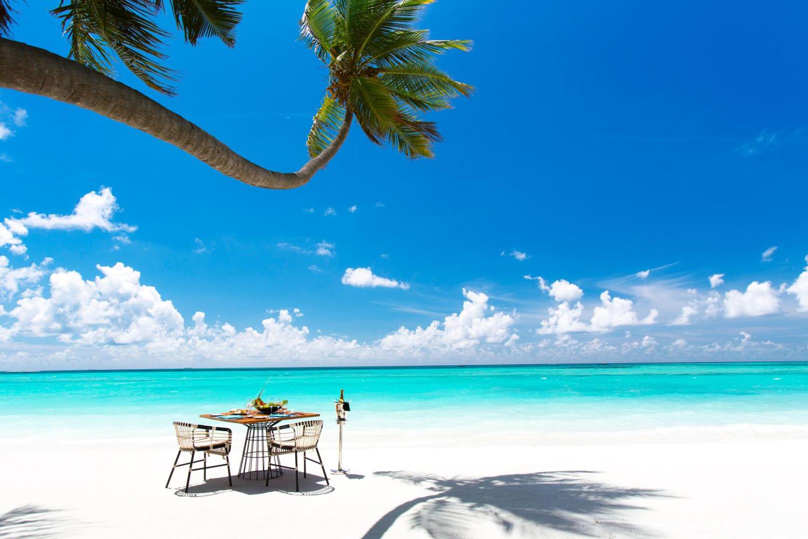 Galdiņš diviem baltu smilšu pludmalē zem noliektas palmas pie tirkīza krāsas okeāna.
