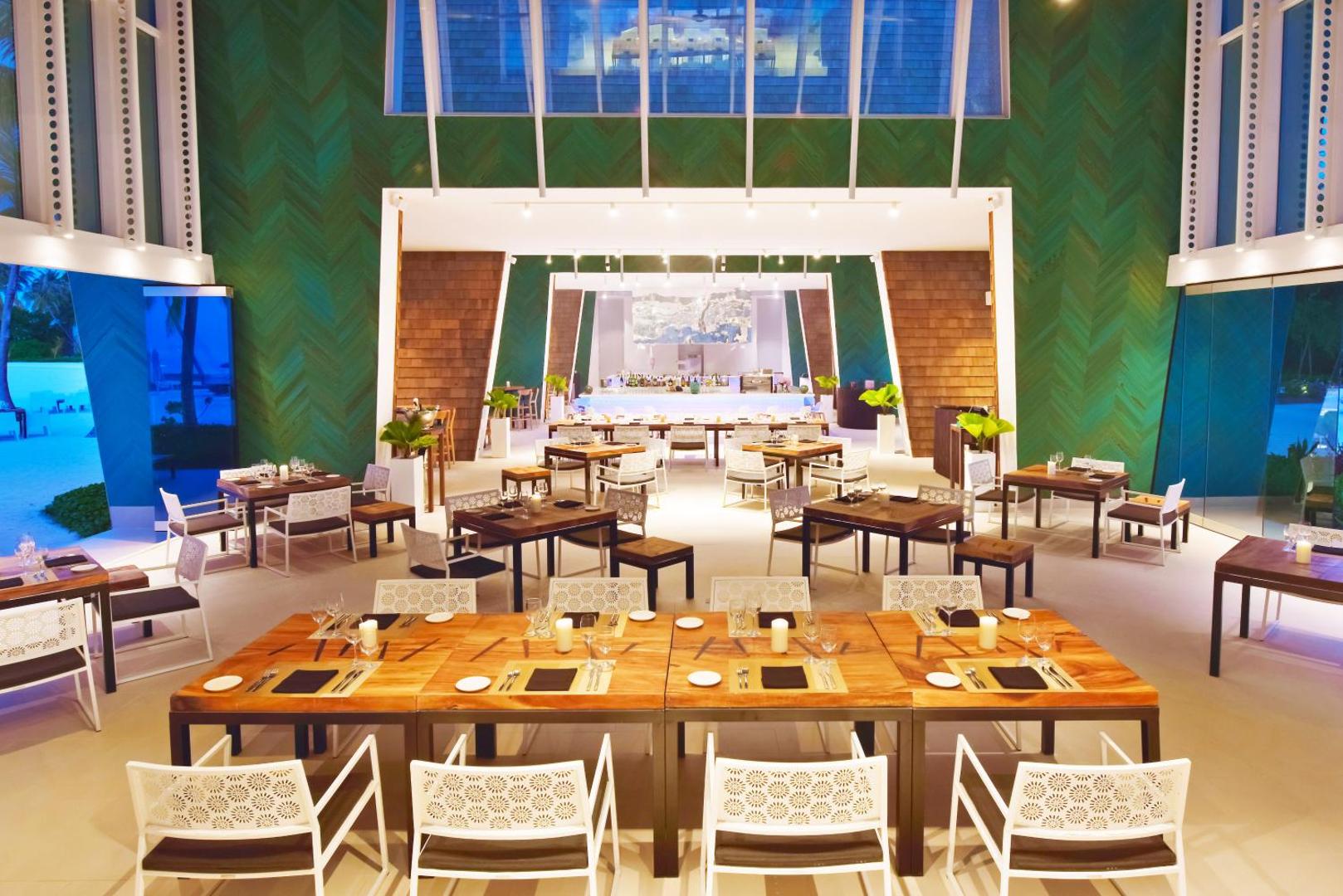 Kandima Maldives restorāns ar koka galdiem un modernu interjeru zaļos toņos.
