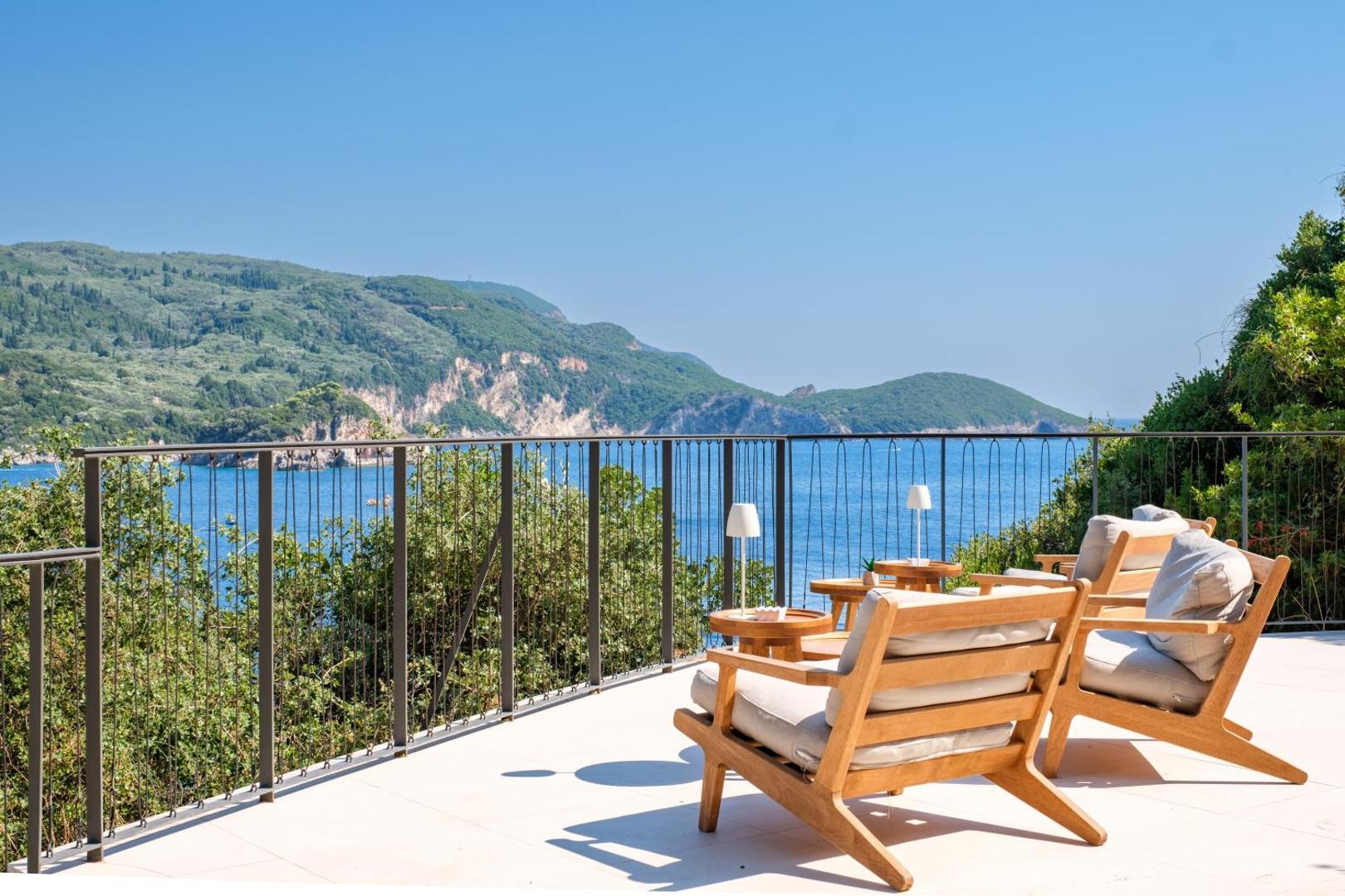 Atpūtas zona uz plašas terases ar koka krēsliem un skatu uz piekrasti.