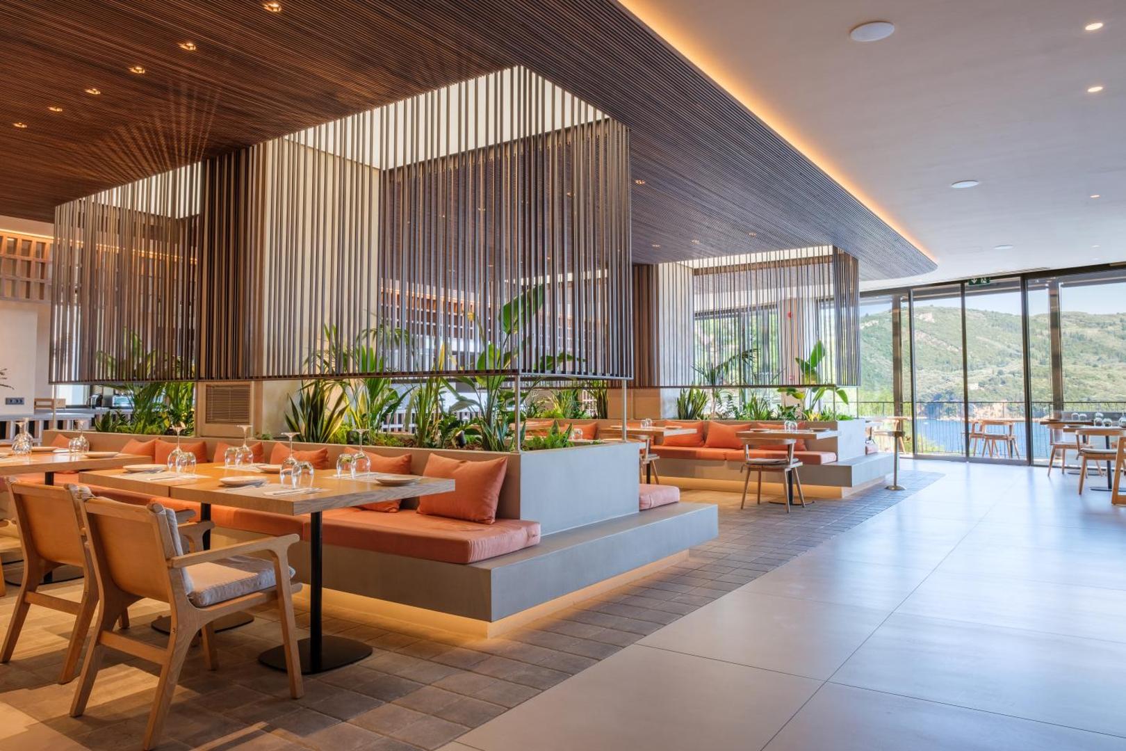 Mūsdienīgs viesnīcas restorāns ar siltu apgaismojumu, koka elementiem un zaļiem augiem.