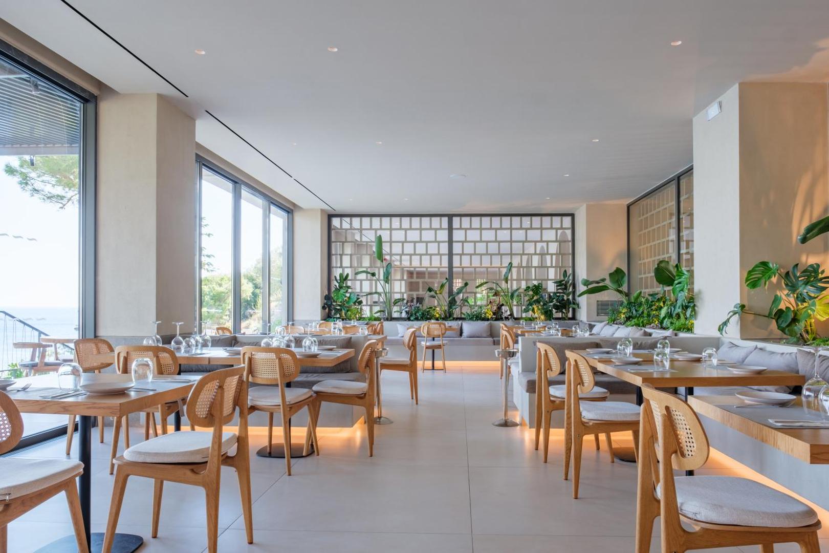 Gaišs un plašs restorāns ar koka mēbelēm un lieliem logiem uz jūru.