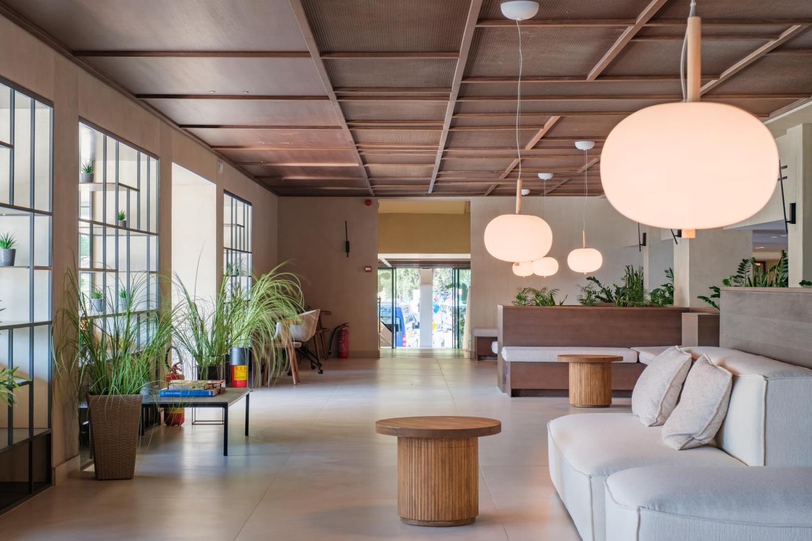 Mūsdienīgs viesnīcas vestibils ar gaišiem dīvāniem, koka galdiņiem un dizaina gaismekļiem.