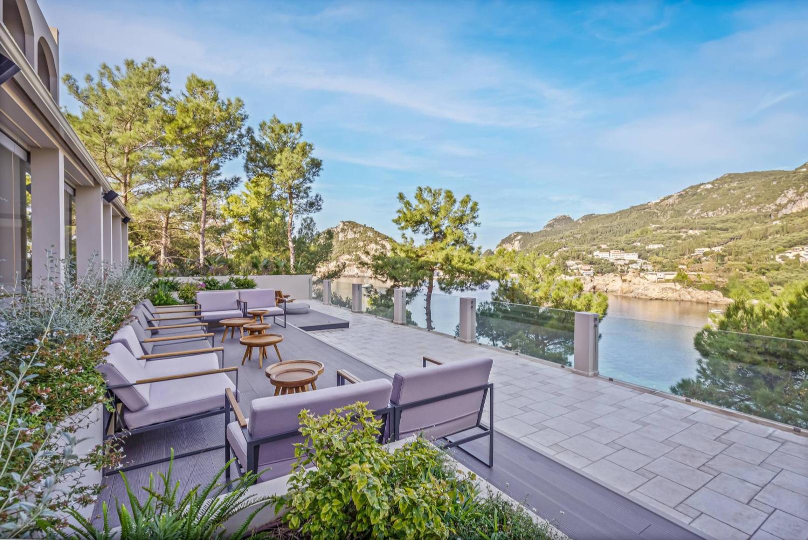Atvērta terase ar ērtiem dīvāniem un skatu uz Paleokastricas līci un kalniem.