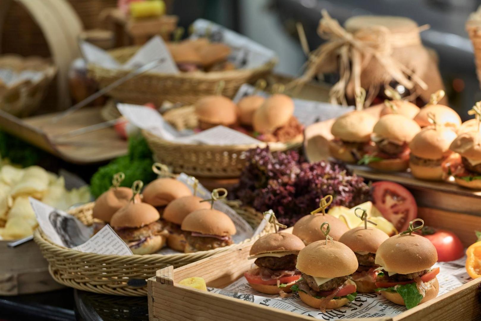 Dažādi mini burgeri un uzkodas servēti pītos grozos un koka paplātēs.