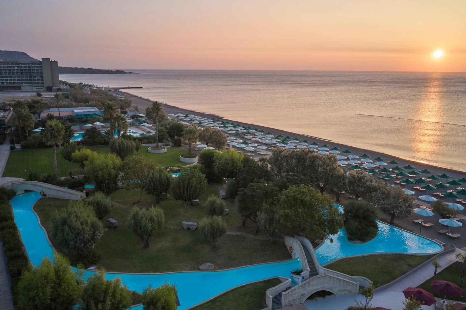 Aerofoto skats uz Esperos Mare Resort & Spa dārzu, lēno upi un pludmali saulrietā.