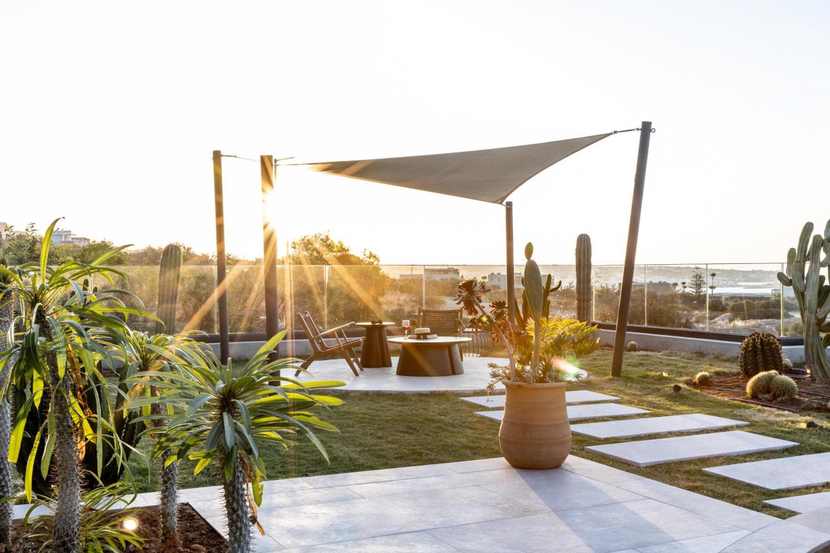 Saulrieta pielieta Elios Hill terase ar atpūtas krēsliem, saules buru un kaktusiem dārzā.