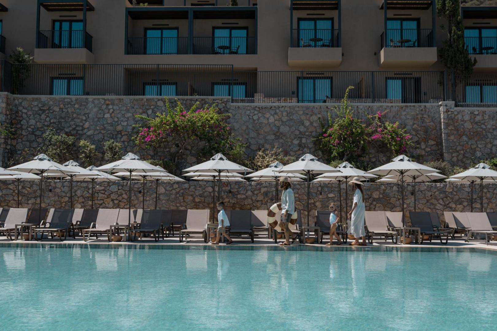 Ģimene pastaigājas gar Elios Hill āra baseinu, ko ieskauj saulessargi un guļamkrēsli.