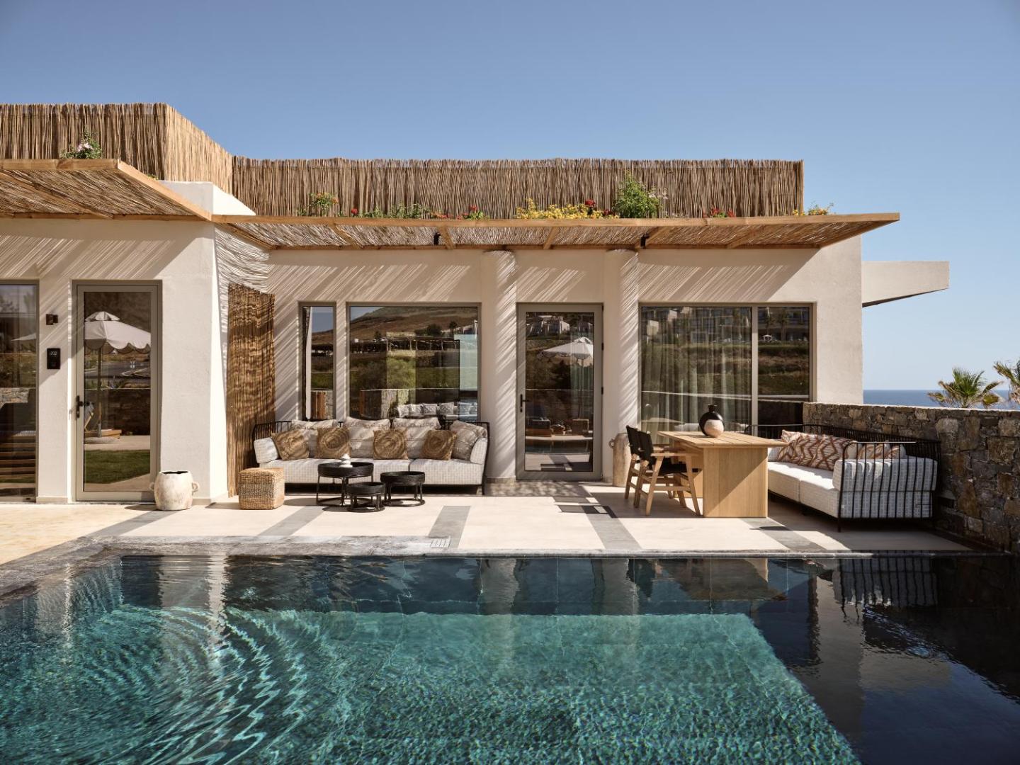 Moderna viesnīcas terase ar privātu baseinu, dīvāniem un koka pusdienu galdu saulainā dienā.