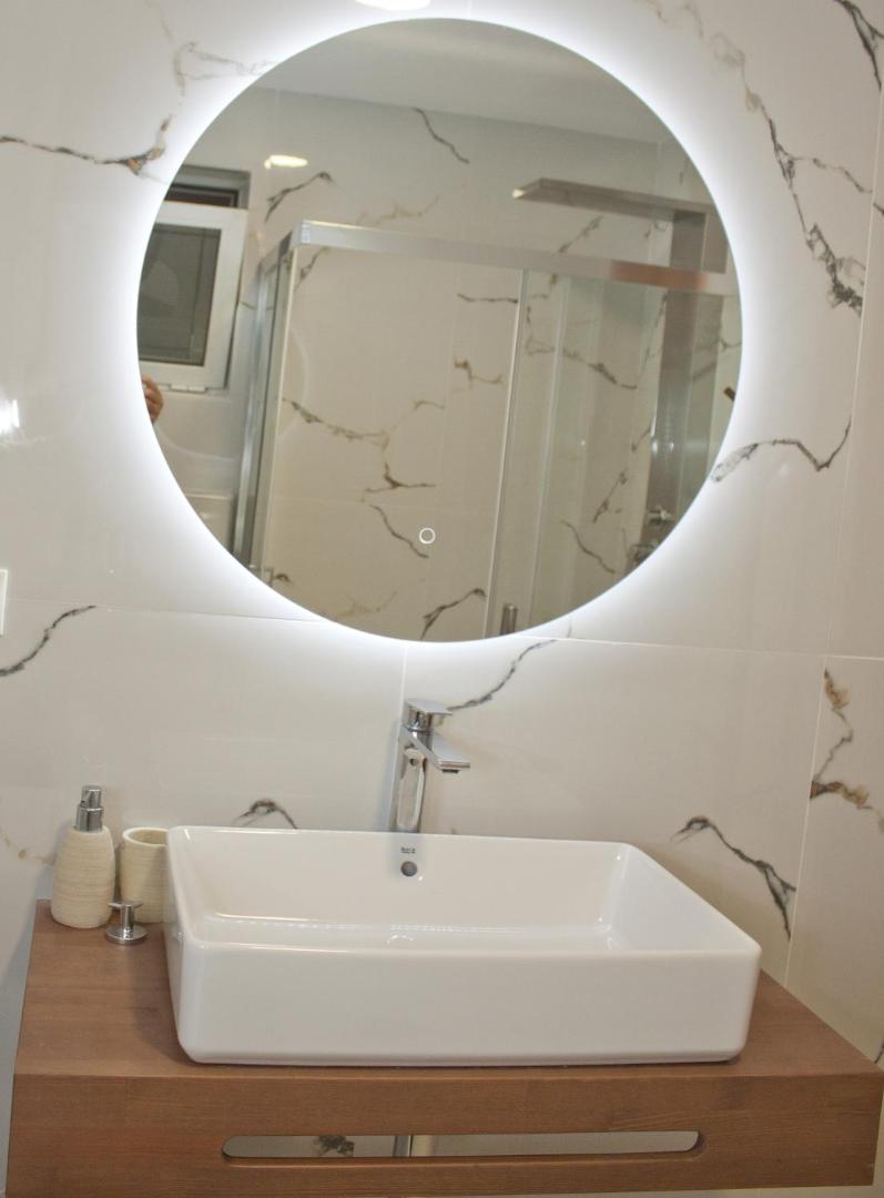 Moderna vannasistaba ar apaļu, izgaismotu spoguli un elegantu izlietni.