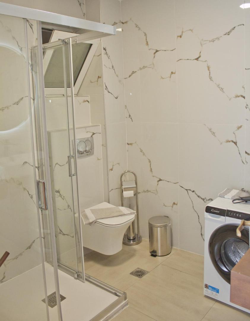 Gaiša vannasistaba ar dušas kabīni, tualeti un veļas mazgājamo mašīnu.