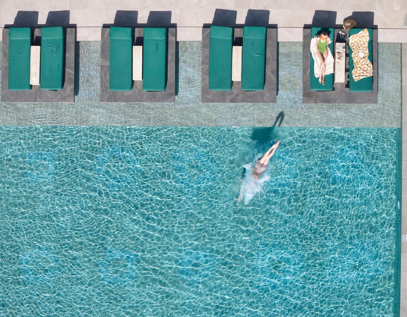 Skats no augšas uz baseinu un sauļošanās zonu ar tirkīza ūdeni.