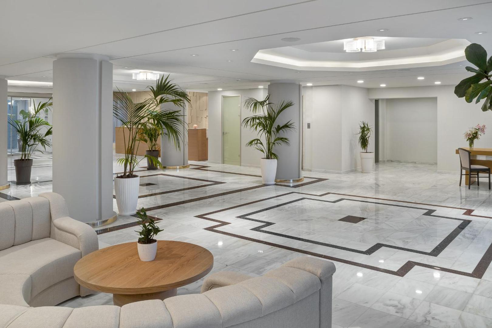 Gaišs un plašs viesnīcas vestibils ar marmora grīdu, kolonnām un ērtiem dīvāniem.