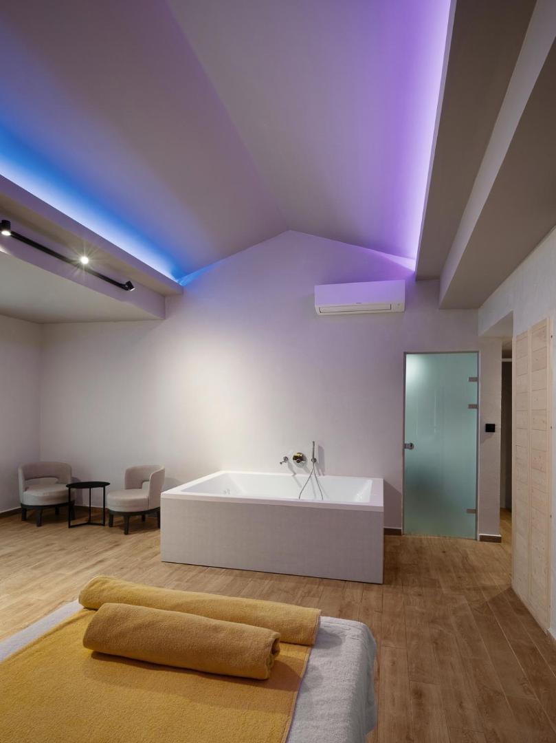 Spa procedūru telpa ar masāžas galdu, lielu vannu un violetu griestu apgaismojumu.