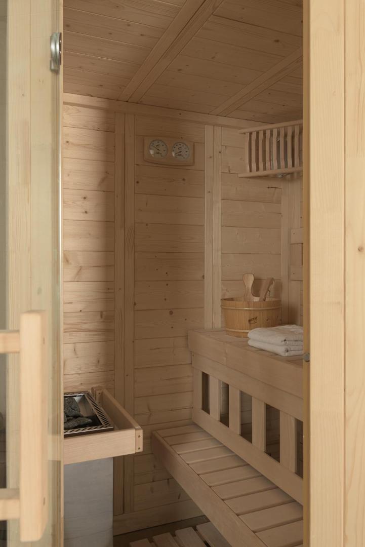 Gaiša koka sauna ar soliem, akmeņu krāsni un koka spaini.